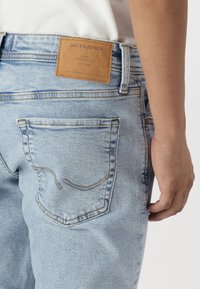 Svijetloplave traperice imaju označenu kožnu etiketu "JACK & JONES." Stražnji džep naglašen je šavovima u zakrivljenom uzorku.