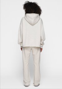 Sudadera oversize de color gris claro con bolsillo canguro y capucha con cordón, combinada con pantalones de pierna ancha a juego. Tejido suave y texturizado.