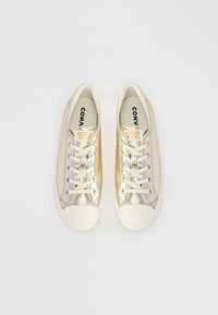 Metallische gouden sneakers met een witte rubberen neuskap, witte veters en branding op de tong. Gladde textuur met contrasterende accenten.
