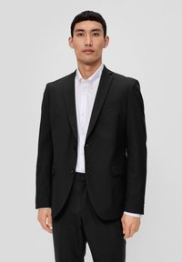 Czarna marynarka w slim fit, z pojedynczym zapięciem na guziki, dwoma guzikami i klapami w kształcie notcha, w zestawieniu z białą koszulą zapinaną na guziki.