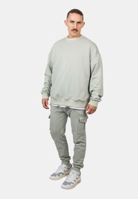 Lys grå sweatshirts med ribbede manchetter og kant, parret med matchende cargo bukser med sidelommer og hvide sneakers med grå detaljer.