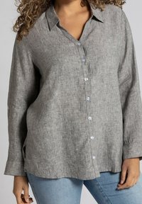 Camicia con bottoni in lino grigia con colletto, maniche lunghe e una vestibilità rilassata. Bottoni trasparenti e spacchi laterali aggiungono dettagli. Abbinata a jeans azzurri chiari.