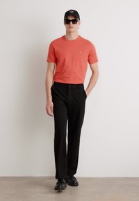 Tricou scurt cu mâneci scurte în culoarea corai, asortat cu pantaloni negri. Ţinuta include o șapcă neagră și ochelari de soare, având un material neted și o croială ajustată.