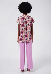 Blusa floreale con stampa multicolore che presenta rose e margherite, abbinata a pantaloni a vita alta di un rosa chiaro. Tessuto dall'aspetto liscio.