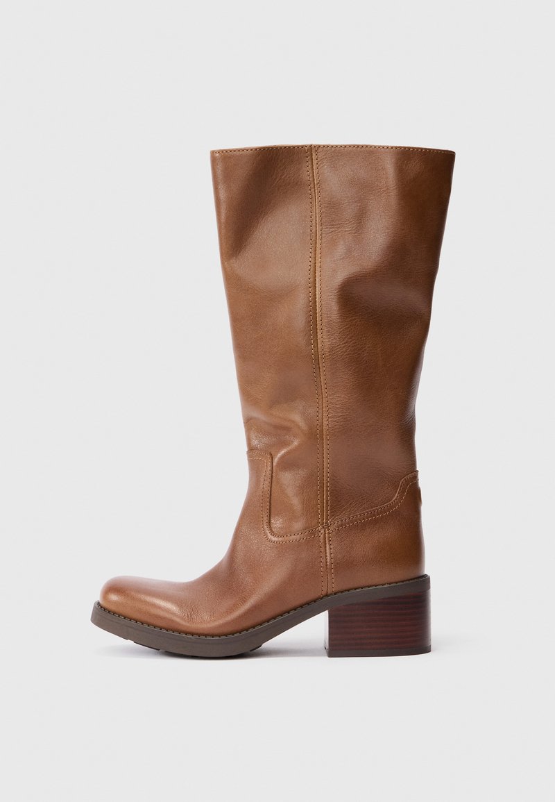 Bota de cuero marrón hasta la rodilla con punta redonda, acabado texturizado y un tacón de madera apilada. Detalle de costura a lo largo de los lados.