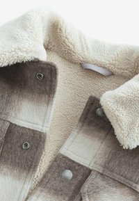 Fleece-lined jacket featuring a checked pattern in shades of gray and cream, with snap buttons and a soft collar.