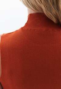 Top senza maniche a collo alto a coste in arancione bruciato. Presenta un design aderente con una texture verticale e una leggera lucentezza.