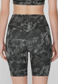 Shorts noirs taille haute avec un motif abstrait gris, fabriqués en tissu extensible. Dotés de coutures plates et d'un empiècement en V à l'arrière.