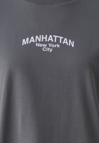 Czarna bawełniana koszulka z okrągłym dekoltem, z białym nadrukiem tekstu: "MANHATTAN Nowe Jork" ułożonym w zakrzywieniu.