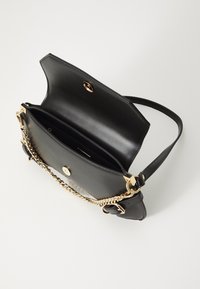 Černá kožená taška s hladkou texturou, zlatými kovovými doplňky a řetízkovým popruhem. Klopa zavírání a viditelné vnitřní přihrádky.