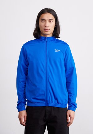 Blue athletic jacket with high collar, full zip closure, and Reebok logo. Features long sleeves and ribbed cuffs. Smooth fabric texture.