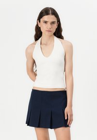 White halter neck top with a deep V-neck design paired with a navy pleated mini skirt, both showcasing smooth textures and fitted shapes.