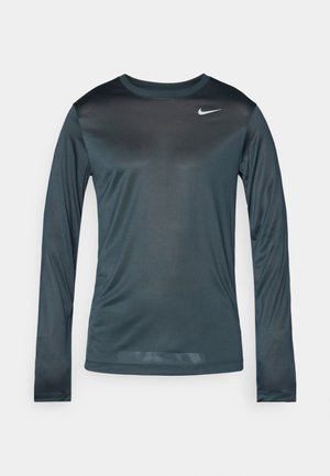 Tumši zaļš sporta krekls ar garām piedurknēm un apaļu apkakli, izgatavots no gludas, vieglas materiāla, ar mazu balto Nike logo uz krūtīm.