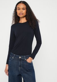 T-shirt azul-marinho de manga comprida, tecido suave, decote redondo, combinado com jeans azul-escuro de pernas largas, com bolsos e detalhes de costura clara.