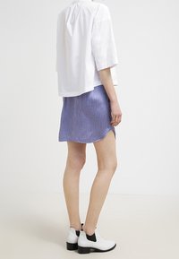 Vit kortärmad topp i kombination med en blå texturerad kjol med en lätt rundad nederkant. Svart- och vitrandiga ankelstövlar fullbordar looken.