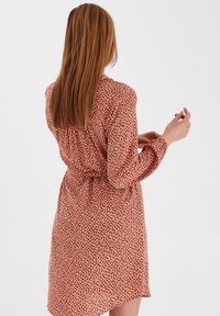 Print skjortklänning i korall med svarta och vita abstrakta prickar, långa ärmar, knytband i midjan och svängd nederkant. Lätt tygtextur.