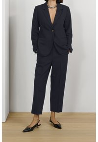 Granatowy garnitur z jednokluczowym żakietem i szerokimi spodniami, zestawiony z czarnymi szpilkami na zapięcie z tyłu. Posiada głęboki dekolt w kształcie litery V.