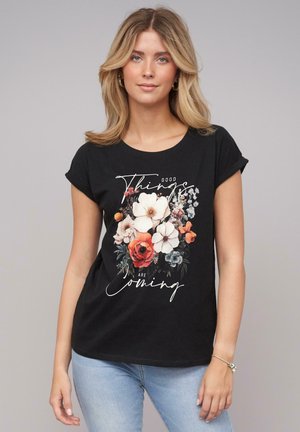 Black cotton t-shirt with a floral print featuring white, orange, and blue flowers, along with the text "Good Things Are Coming."