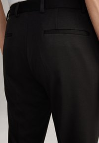 Schwarze maßgeschneiderte Hose mit glatter Textur, schlankem Schnitt, zwei Gesäßtaschen und einem schlichten Bunddesign.