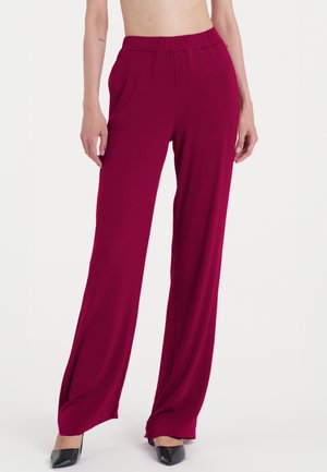 Pantaloni ampi bordeaux con una texture liscia, vita elastica e tasche laterali. Abbinati a décolleté nere a punta.
