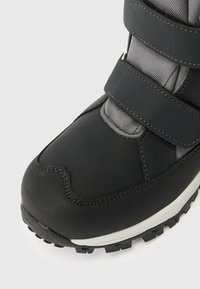 Černé a šedé tenisky s vysokým obvodem, s texturovanou podrážkou a dvěma nastavovacími pásky na suchý zip pro bezpečné uchycení, zobrazené zblízka.