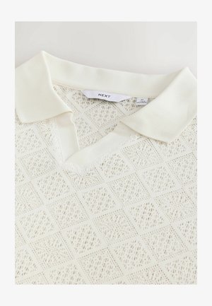 Polo shirt en maille blanche texturée avec un col en V, présentant un col côtelé et des détails en motif losange. Étiquette de marque "NEXT" visible.