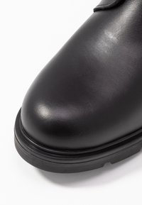 Stivale alla caviglia in pelle nera con punta rotonda, texture liscia e suola in gomma con un sottile dettaglio di bordo esterno.