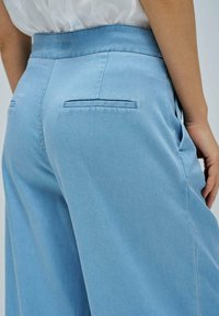 Pantalons en denim de couleur bleu clair avec taille haute, poches latérales et poches arrière cousues. Texture lisse et coupe large.