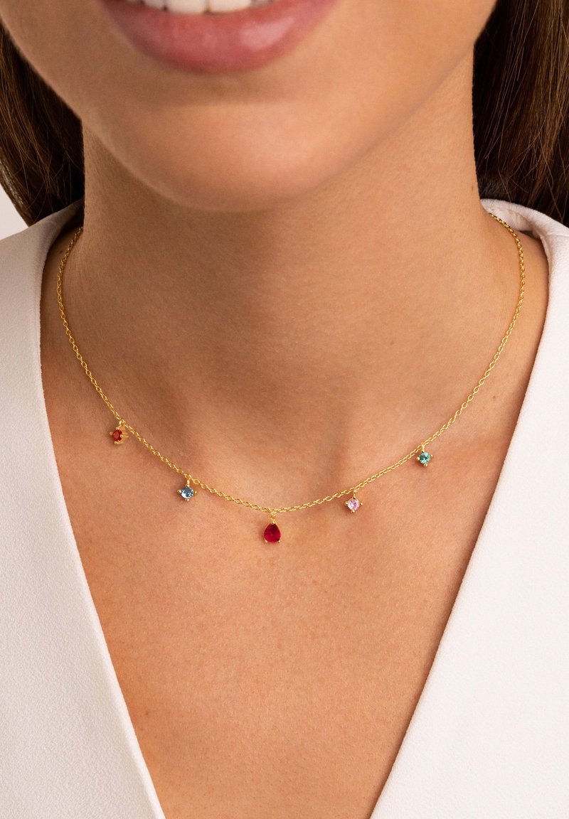 Goldfarbene, gedrehte Kettenhalskette mit fünf mehrfarbigen Edelsteinhängern: rot, blau und pink. Einfaches Design, nahe am Schlüsselbein.