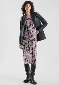 Czarna skórzana marynarka na fioletowo-różowej sukience midi w stylu tie-dye z marszczeniami, zestawiona z czarnymi skórzanymi kozakami na obcasie do kolan. Gładka faktura i dopasowany krój.