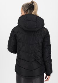 Giacca a vento nera in tessuto trapuntato orizzontale, con cappuccio staccabile e logo marrone sulla parte posteriore. Materiale caldo e isolante.