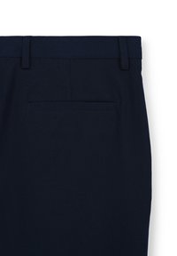 Marineblaue Anzughose, die den hinteren Bund mit Gürtelschlaufen und einer einzelnen Paspeltasche vor einem weißen Hintergrund zeigt.