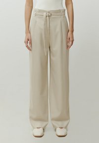 Beige gemusterte weite Hose mit einem taillierten Bund, die ein Hahnentrittmuster und eine glatte Stofftextur aufweist.