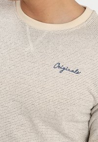 Sudadera de rayas crema con un cuello redondo acanalado y mangas con puños, con bordado en azul oscuro que dice "Originals" en el pecho.