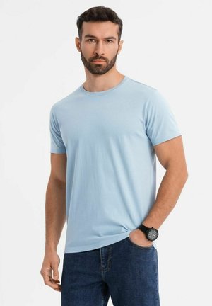 Camiseta de manga corta de color azul claro en tejido suave, con escote redondo, combinada con jeans de mezclilla oscuros, acompañada de un reloj de pulsera negro.