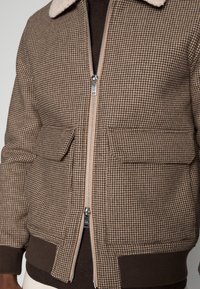 Hnědá houndstooth bomberská bunda s kožichem, zapínání na zip a dvěma předními kapsami; žebrované manžety a spodní lem.