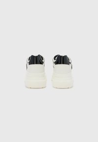 Zapatillas negras y blancas con un upper texturizado, que presentan un acento brillante en el talón negro y una gruesa suela blanca.