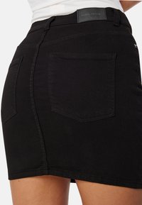 Černá džínová mini sukně s přiléhavým střihem, dvěma zadními kapsami a diskrétní značkovou visačkou na pasu. Hladká textura.