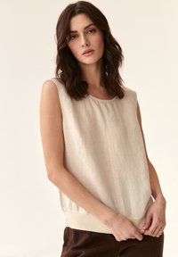 Beidzamais bez piedurknēm topiņš ar apaļu kakla izgriezumu un maigu tekstūru; tam ir kontrastējošs apakšmala un brīvs griezums. Vienkāršs, minimālistisks dizains.