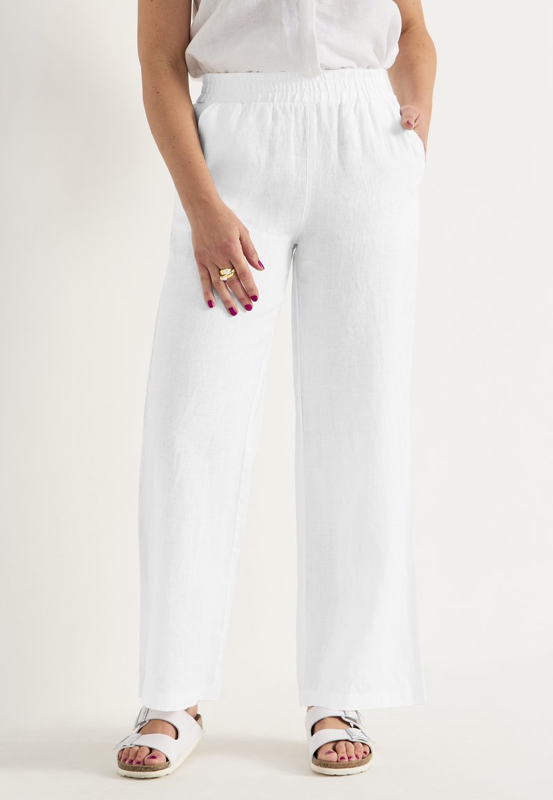 Witte linnen wijde broek met een elastische tailleband, twee zijzakken en een gestructureerde stof. Gecombineerd met lichtgekleurde sandalen.