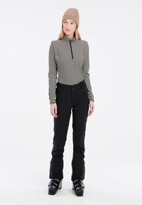 Schwarze Skihose mit zwei Seitentaschen, kombiniert mit einem gestreiften Langarmoberteil mit einem Reißverschlusskragen und einer beigen Strickmütze.