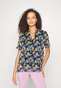 Blusa floral com fundo azul-marinho, mangas curtas, decote em V, apresentando flores amarelas e azuis claras, tecido suave e corte solto.