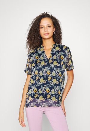 Blusa floral com fundo azul-marinho, mangas curtas, decote em V, apresentando flores amarelas e azuis claras, tecido suave e corte solto.