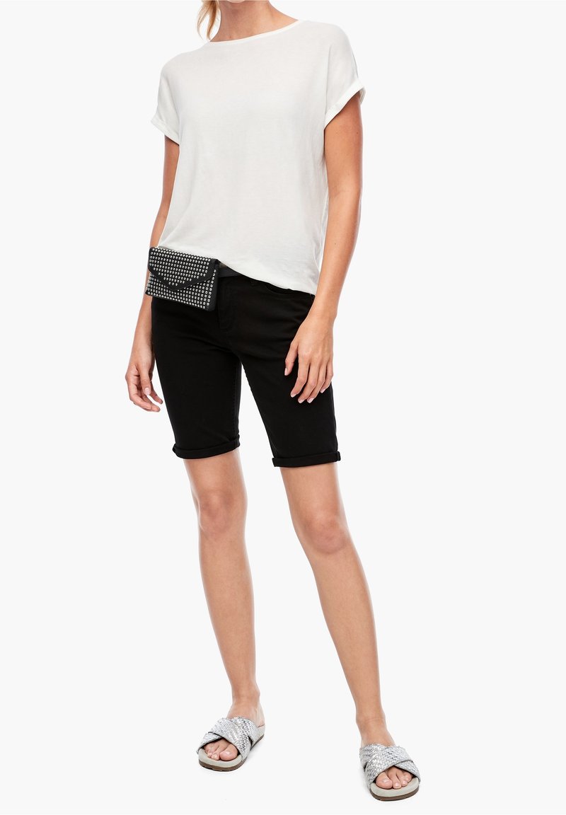 Top bianco a maniche corte, pantaloni corti neri fino al ginocchio e sandali texturizzati argento. Una borsa da cintura nera con tessuto e borchie argento completa l'outfit.