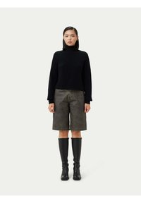 Svart stickad polotröja i kombination med oliogröna shorts. Modellen bär knähöga svarta stövlar. Enkel, modern design med texturerad tyg.