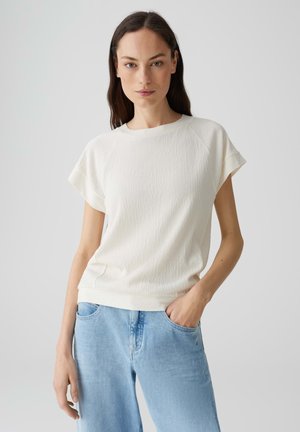 Crème-kleurig, gestructureerd shirt met korte mouwen en een ronde halslijn, gecombineerd met lichtblauwe denim jeans.
