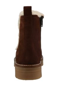 Brązowy zamszowy botek za kostkę z futrzanym wykończeniem, tylnym zamkiem i gumową podeszwą. Posiada pętelkę przy pięcie dla łatwego zakładania.
