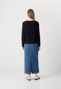Črna dolgosleeve majica v kombinaciji z modrim denim maxi krilom, ki ima dve zadnji žepki in srednji zadnji razporek, obuta v bež slip-on čevlje.