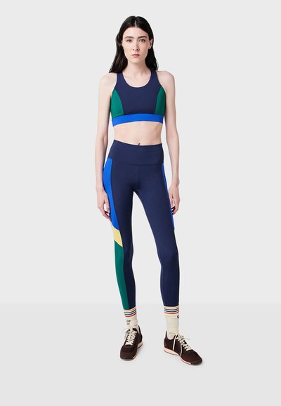 Námořnická sportovní podprsenka se zelenými a modrými akcenty v kombinaci s námořnickými legínami s výraznými vícoloré panely a hladkým povrchem.
