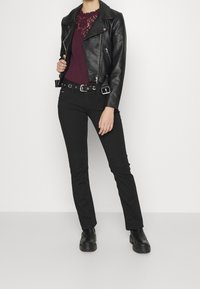Giacca da biker nera in pelle sopra un top borgogna bordato in pizzo, abbinato a pantaloni neri slim-fit e stivaletti neri. La cintura presenta dettagli metallici.